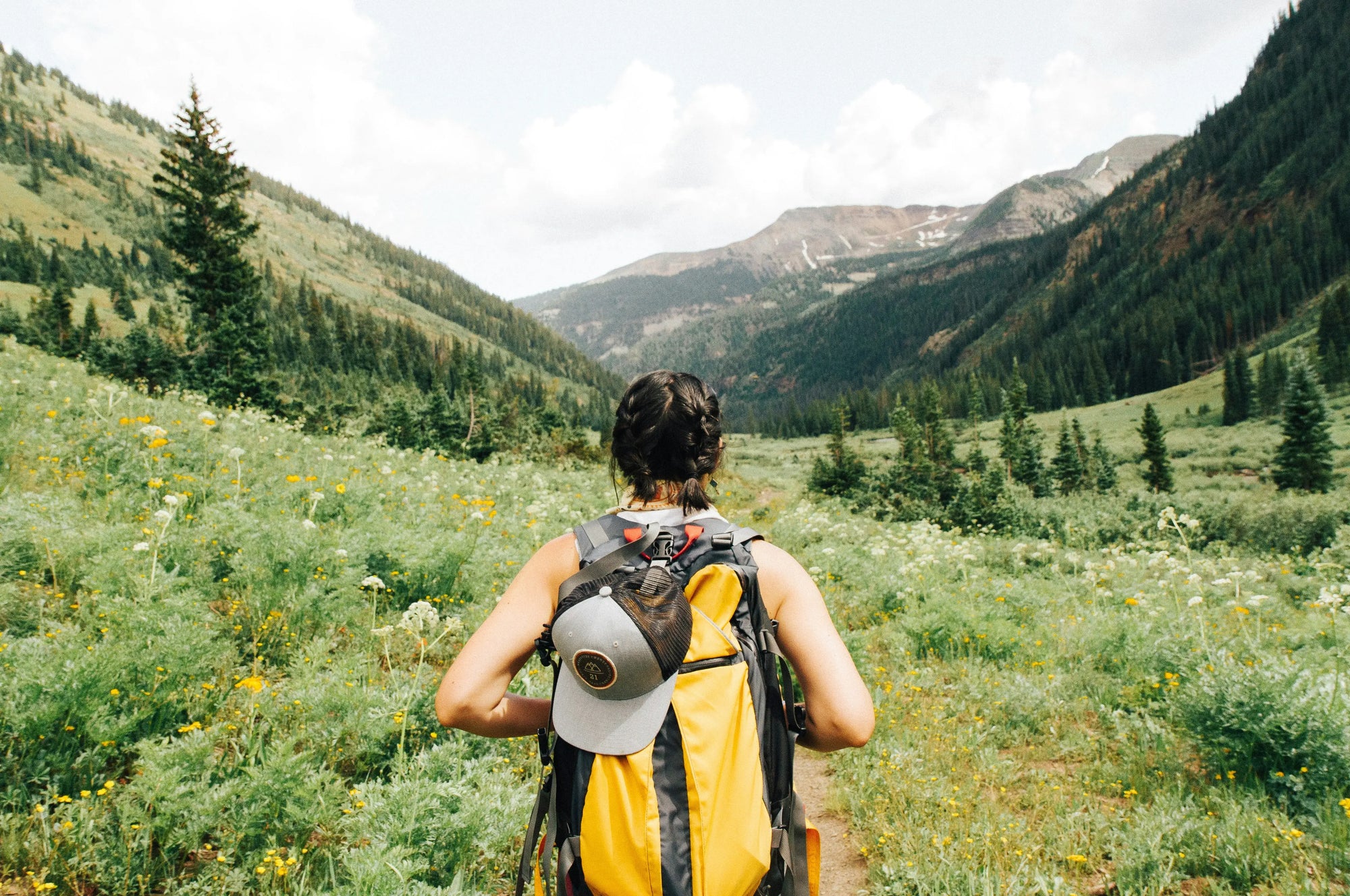 A traveler smiles while applying no-rinse body wash to their arm in a scenic outdoor setting, with a backpack and hiking boots visible in the background.